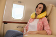 © New Africa - Young woman with travel pillow sleeping in airplane during flight