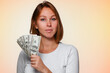 Portrait of a pretty woman holding a fan of American dollars in her hand. Beige background. The concept of finance and succes