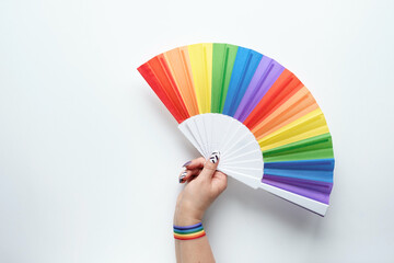 LGBTQ community pride. Hand holds. rainbow fan. Ribbon with rainbow design on wrist. Flat lay, top view on off white paper. Simple, minimal LGBT pride flag colors decor.