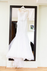 Canvas Print - Vertical shot of a bridal dress on a hanger over a tall mirror