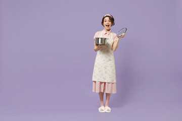 Full length amazed young fun housewife housekeeper chef cook baker woman in pink apron hold soup stainless pan saucepan look camera isolated on pastel violet background Cooking food process concept