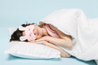 Full length young sleeping woman 20s wear pajamas jam sleep mask rest relax at home lying lies wrap cover blanket duvet on pillow isolated on pastel blue background. Good mood night bedtime concept.