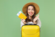 Close up excited tourist woman in casual clothes hat hold passport tickets yellow suitcase spread arms isolated on green background Passenger travel abroad weekend getaway Air flight journey concept