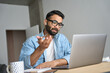 canvas print picture - Young eastern indian Hispanic male teacher wearing glasses with earphones having webinar video training class using laptop at modern home office. Remote distant online work e learning tech concept.