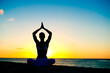 © TRAVEL EASY - Woman meditating, doing yoga, at the beach, sitting by the seashore, dressed in a white outfit at sunset