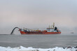 Vessel engaged in dredging at sunset time. Hopper dredger working at sea. Ship excavating material from a water environment.