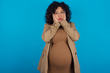 young Arab pregnant woman wearing dress against blue wall Tired hands covering face, depression and sadness, upset and irritated for problem