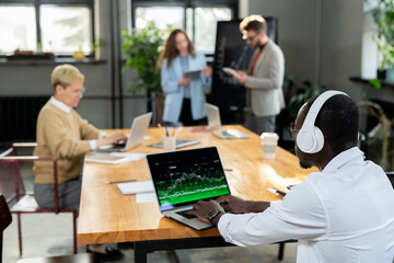 Canvas Print - African businessman in headphones working with online data against colleagues