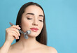 © New Africa - Woman using metal face roller on light grey  background, space for text