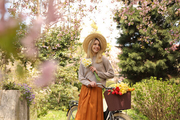 Wall Mural - Beautiful young woman with bicycle and flowers in park on pleasant spring day