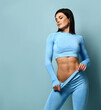 Fitness girl portrait. Woman in fashion sportswear, standing on a blue background, after a workout. Girls with a strong muscular body come up, show their pumped up abs.