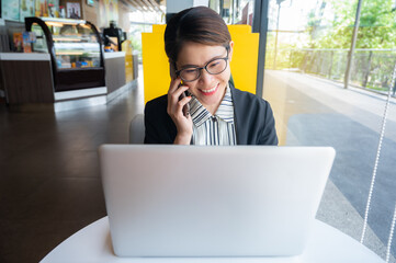 Portrait of young Asian businesswoman working on laptop while talking to someone on phone. Conceptual shot of businesswoman lifestyle while working.