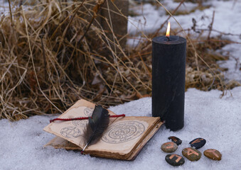 Wall Mural - Magic ritual with black candle, runes on stones and open with book with spells on snow.