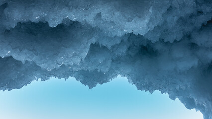 The vault of the grotto in the rock is covered with layers of icicles, like lace frills. Transparent blue ice against the azure sky. Close-up. Full screen. Baikal