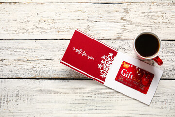 Gift card and cup of coffee on light wooden background