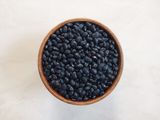 Seeds black beans (Vigna mungo) in wooden bowl on white cement floor.