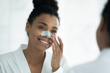 happy beautiful african american woman applying cleansing strip on nose, sticking patch for removing