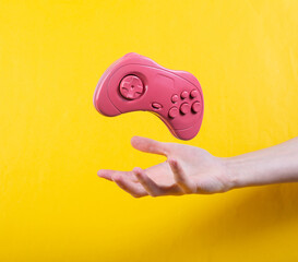 Canvas Print - Hand and Levitating pink gamepad on yellow background. Minimalistic still life. Concept art. Video game