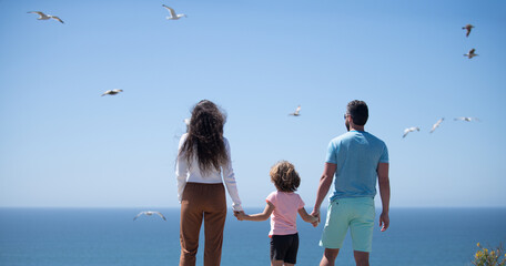 Wall Mural - Happy family holidays. Joyful father, mother, baby son walk of sea sand beach. Active parents and people outdoor activity on summer vacations with children. Childhood and parenting concept.