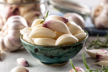 Wall Mural - Aromatic garlic cloves filled in blue rustic bowl with savory rosemary as a decoration and more garlic in the background