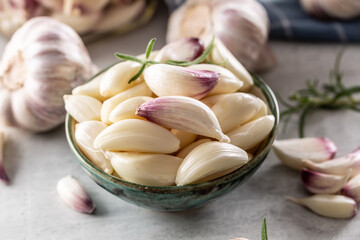 Wall Mural - Aromatic garlic cloves filled in blue rustic bowl with savory rosemary as a decoration and more garlic in the background