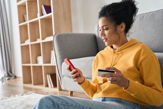 young adult african american female consumer holding credit card and smartphone sitting on floor at 