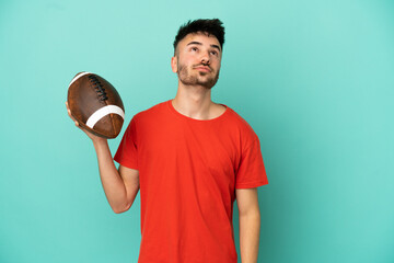 Wall Mural - Young Caucasian man playing rugby isolated on blue background and looking up