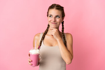 Wall Mural - Young woman with strawberry milkshake isolated on pink background and looking up