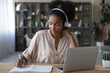 © fizkes - Happy young african american woman in wireless headphones listening educational online lecture, writing down important information. Smart mixed race student involved in online study by video zoom call