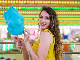 Mujer joven disfrutando de un algodón de azúcar en la feria o parque de atracciones