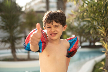 Wall Mural - Boy with muffs looking at camera in his garden pool