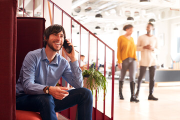 Wall Mural - Businessman On Phone Sitting By Stairs In Modern Open Plan Office 