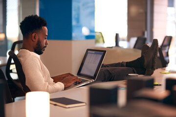 Wall Mural - Young Businessman Working Late Sitting At Desk With Laptop In Modern Open Plan Office