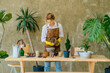 © Iryna - Process of preparing for plant transplantation. Attractive woman in yellow household gloves holding pour over drainage for houseplants at pot on wooden table. Eco concept. Eco hobby.