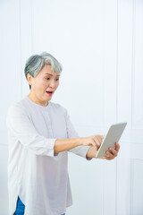 Wall Mural - Smiling middle-aged Asia woman browsing wireless Internet on tablet at home, happy modern senior female using pad device, elderly technology concept.