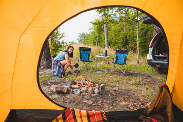 Wall Mural - view from camping tent woman cooking on burner near bonfire