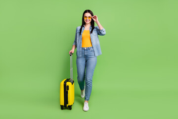 Full size photo of happy beautiful girl in sunglass go walk in airport with luggage isolated on green color background