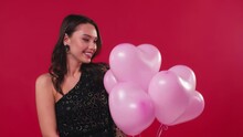 Flattered Woman In Black Dress Receiving Pink Balloons Isolated On Red