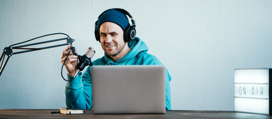 Wall Mural - Cheerful host streaming his audio podcast at small and cozy home broadcast studio