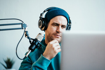 Wall Mural - Cheerful host streaming his audio podcast at small and cozy home broadcast studio