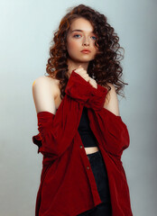 Attractive brunette with long curly hair. Female fashion model with wavy hairstyle in a red shirt posing on a gray background