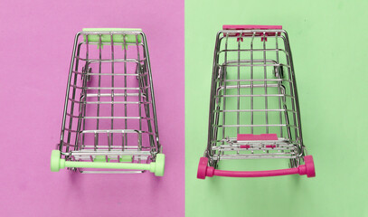 Wall Mural - Two mini supermarket trolleys on blue pink pastel background. Shopping concept. Top view. Minimalism