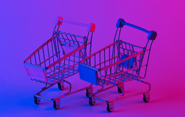 Two shopping trolley in trendy neon light. Gradient pink-blue glow. Concept art. Minimalism