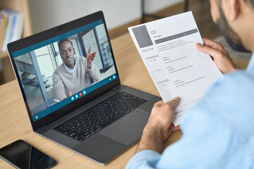 Wall Mural - Young indian confident businessman holding cv talking to male black man potential employee hiring for job. Virtual video call between employer and manager worker. Remote recruitment work concept.