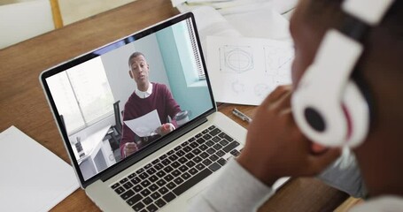 Canvas Print - African american male college student holding notes while having a video call on laptop at home