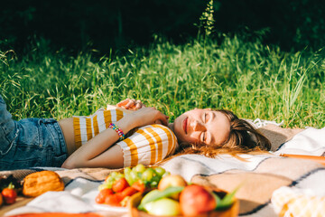 Wall Mural - Young cheerful woman with closed eyes lying on picnic blanket enjoying summer weather, in natural park, holidays vacation.