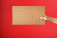 Hand Holding A Blank Sheet Of Cardboard On A Red Background.