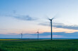 © Gabriel - Dramatic landscape of wind power stations in a wind farm with propellers moving against the background of blue and orange sky during sunset.