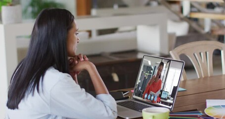 Poster - Mixed race businesswoman sitting at table using laptop having video call with female colleague