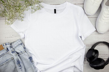 white womens cotton tshirt mockup with flowers, jeans, sneakers and black headphones on wooden backg